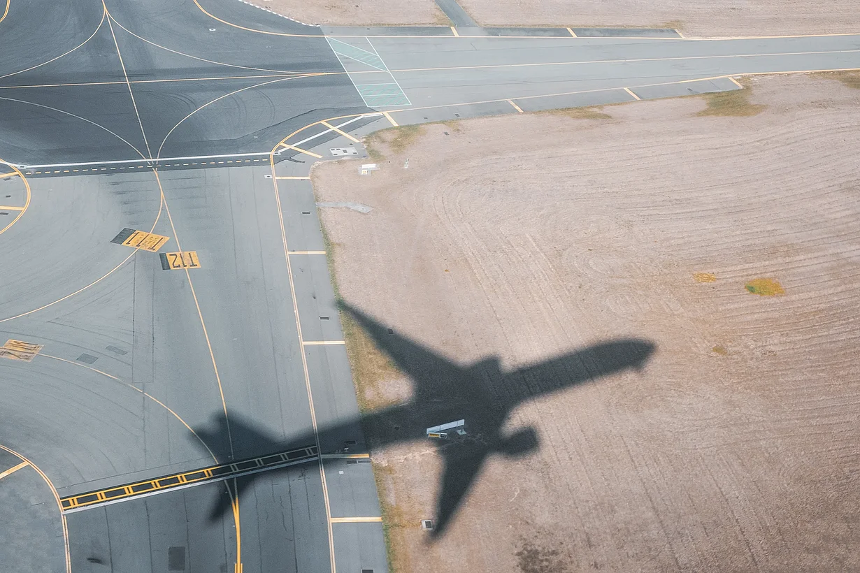Schatten eines abhebenden Flugzeugs auf dem Boden eines Flughafens.